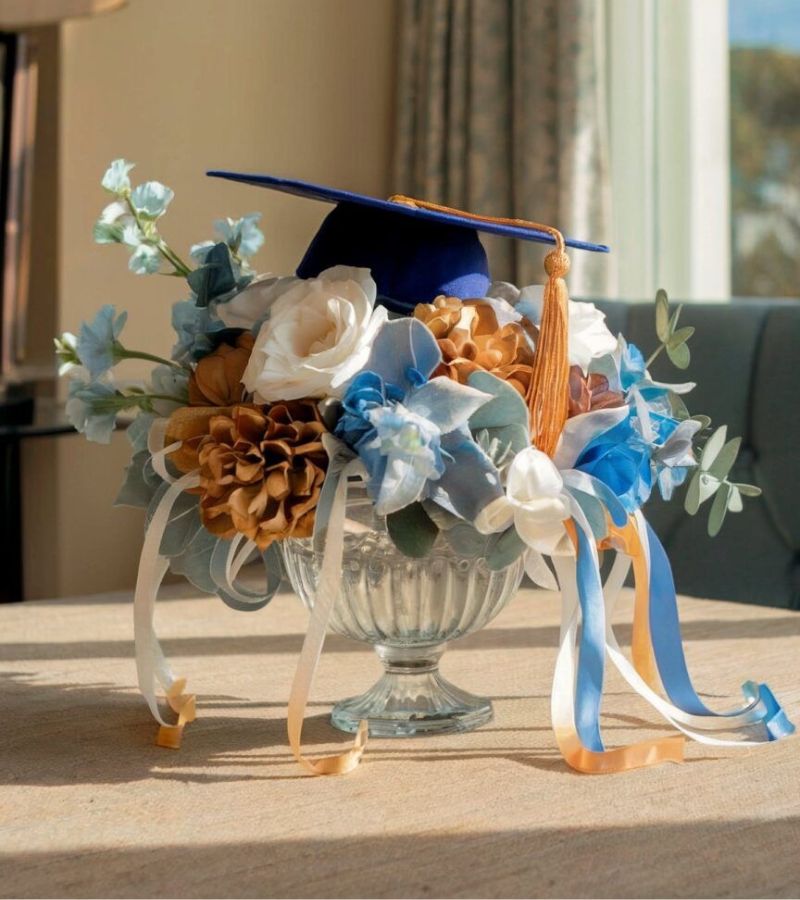 blue theme graduation party centerpieces - blue vase with blue and white flowers inside and a blue graduation cap on top