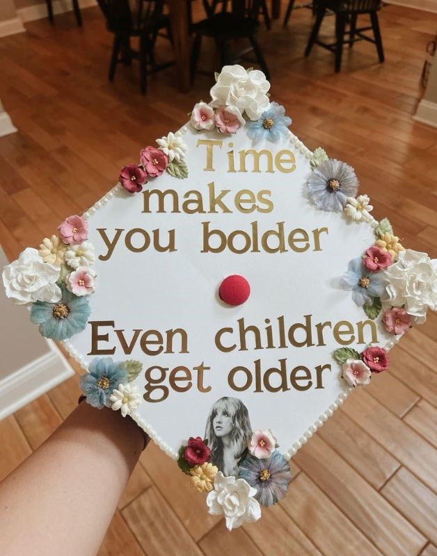 white graduation cap design saying time makes your bolder even children get older with florals on the corners